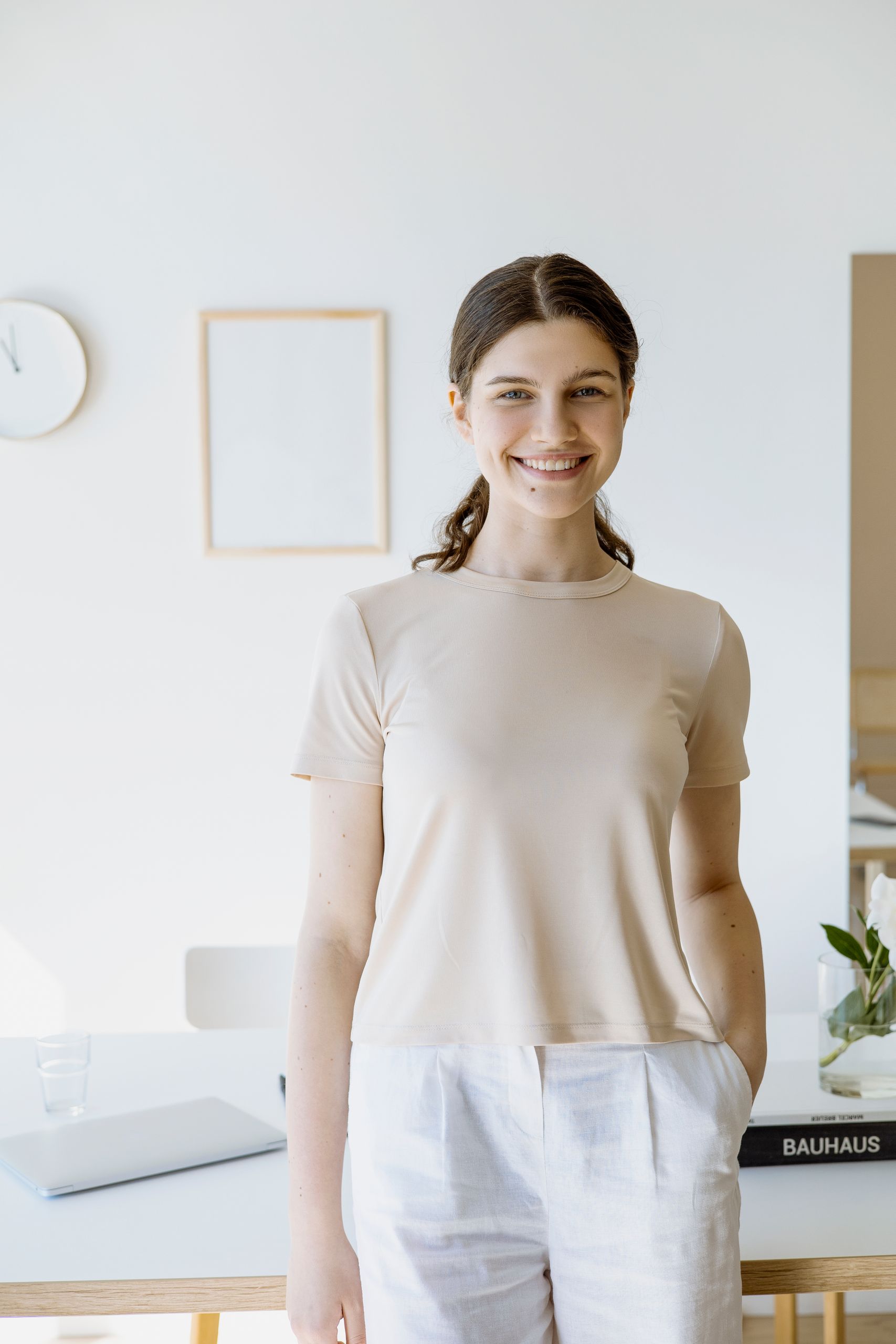A young woman smiling indoors in a minimalist room, emitting a warm and inviting vibe.